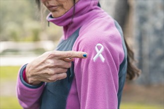 Mid adult woman pointing to an embroidered cancer awareness ribbon with her finger on her sweatshirt
