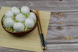 Xiao long bao of prawns on a bed of lettuce in a wooden bowl with chopsticks and a ceramic spoon with soy sauce