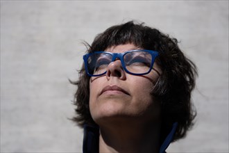 Headshot on a Elegant Woman with Eyeglasses and Looking Up and Leaning on a Concrete Wall in a Sunny Day in Switzerland