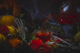 Pouring tea into glass cup surrounded by Halloween decorations