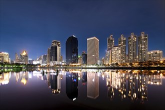 Beautiful landscape with modern high-rise buildings reflecting in calm lake waters at night. Benjakitti Park