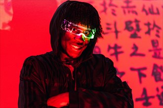 Studio portrait with red neon lights of a friendly futuristic afro man with AR goggles