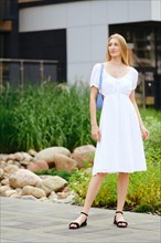 Young woman in white sundress waiting for taxi in townhouse