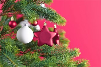 Close up of decorated Christmas tree with pink star shaped and white ball shaped tree ornament baubles on pink background
