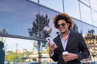 Cool businessman with sunglasses using phone standing in a financial district