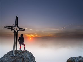 Mountaineer at the summit cross Hohe Goell at sunrise