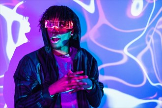 Studio portrait with purple and blue neon lights of an amazed futuristic afro man wearing an augmented reality goggles