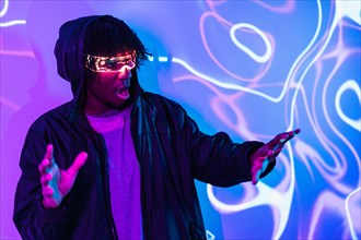 Studio portrait with purple and blue neon lights of a shocked afro man using augmented reality goggles