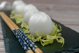 Xiao long bao of prawns on a bed of lettuce on a slate plate with chopsticks and a ceramic spoon with soy sauce