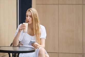 Young woman drinking raf coffee and holding smartphone in hand