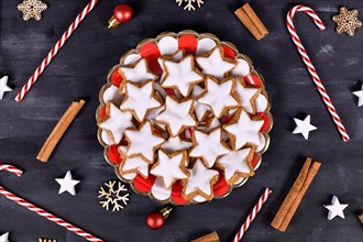 German star shaped glazed cinnamon Christmas cookies called 'Zimtsterne' on striped plate surrounded by cinnamon sticks and seasonal decoration