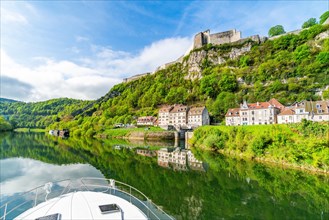 View from the bow of a houseboat on houses at the foot of the Saint Etienne mountain with the world heritage site of the citadel of Besancon on the river Doubs