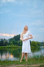 Dreamy young woman by the river in the evening
