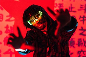 Studio portrait with red neon lights of a futuristic man wearing smart glasses gesturing and looking at camera