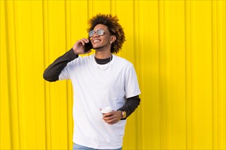 Horizontal photo with yellow background of a man with afro hairstyle talking to the mobile outdoors