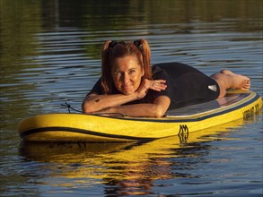 Woman lying relaxed on standup paddle board in lake
