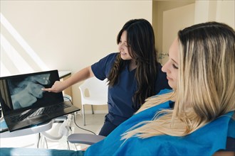 Female dentist shows the x-ray on the laptop to her patient. A dentist using technology to show an x-ray