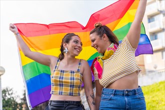 A closeup shot of two young Caucasian females holding high LGBT pride flag outdoors