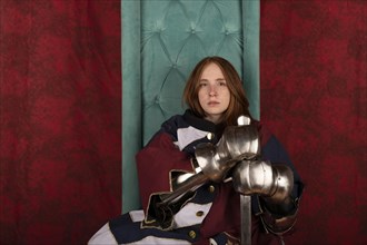 History of the Middle Ages. Portrait of a beautiful medieval knight in armor sitting on a throne on a red background