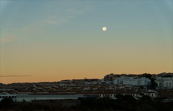 Sunrise cityscape with reddish and blue tones with a full moon in the sky in ronda