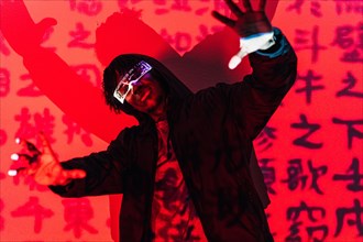 Studio portrait with red neon lights of a cool man with augmented reality goggles dancing