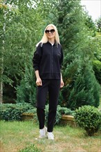 Sporty woman in black hoodie and fleece trousers walking in the garden