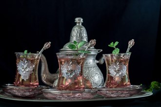 Close-up of a traditional Moorish mint tea service on a tray with decorated glass tableware and silver teapot and sugar bowl