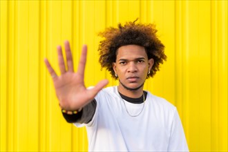 Horizontal photo with yellow background of a Mixed-raced young man gesturing stop with the hand