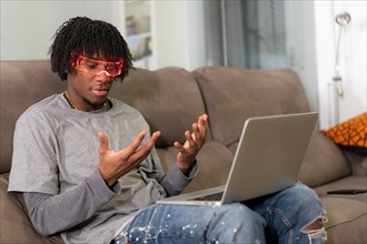 Amazed man using augmented reality goggles sitting on the sofa with a laptop on the lap at home