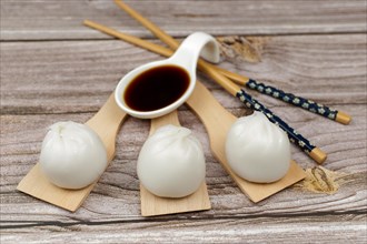 Xiao long bao of prawns on wooden spoons with chopsticks and a ceramic spoon with soy sauce