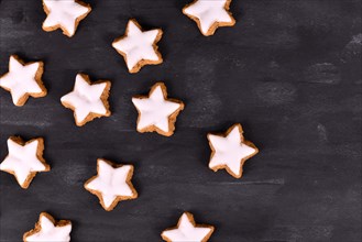 German star shaped glazed cinnamon Christmas cookies called 'Zimtsterne' on dark black background