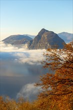 Mountain Peak San Salvatore Above Cloudscape with a Autumn Tree and Sunlight with Clear Sky in Lugano