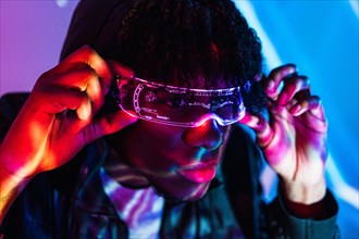 Studio portrait with purple and blue neon lights of an afro man adjusting his artificial intelligence goggles