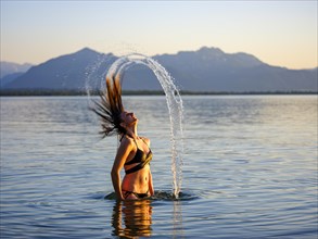 Young woman in the water throws back her long hair with a surge of water
