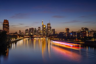 A ship sails on the Main towards Frankfurt's glowing bank skyline in the evening.