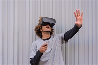 Horizontal photo with urban grey background of an african american men gesturing while using virtual reality goggles