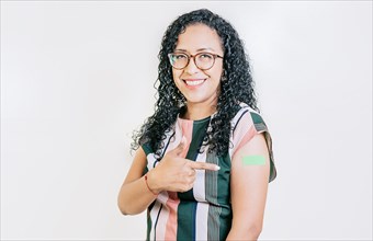 Latin woman pointing at the bandage on her vaccinated arm isolated. Smiling woman pointing at her vaccinated arm