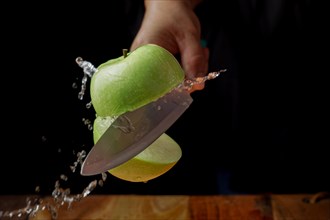 Woman cutting an apple in half with a knife in the air spilling water