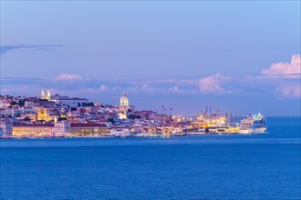 View of Lisbon over Tagus river with moored cruise liner in evening twilight. Lisbon