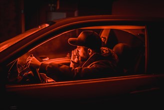 Man in car smoking at night in a garage lit with a red light