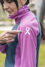 Mid adult woman pointing to an embroidered cancer awareness ribbon with her finger on her sweatshirt. Vertical shot
