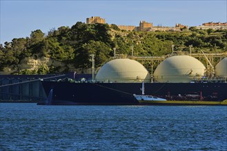 LNG or liquified natural gas tanker moored by industrial pier and green hill on sunny day. Alternative gas supply