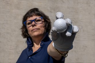 Female Golfer with Eyeglasses and a Glove Holding Up Her Golf Ball and Looking at Camera in a Sunny Day in Switzerland