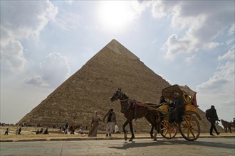 Two-wheeled horse-drawn carriage passes in front of a pyramid