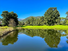 Golf Course with Water Pond and Reflection and Mountain in a Sunny Summer Day in Lugano