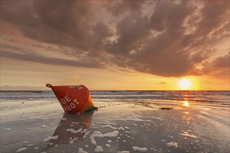 Seascape showing orange buoy on the beach at low tide and sunset over the Wadden Sea