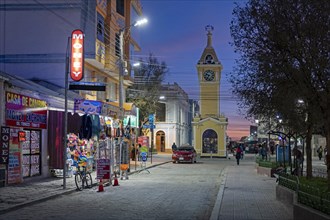 Shops in the main street and yellow clock tower in the city Uyuni after sunset