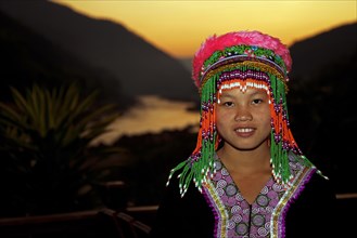 Traditional tribal dancer wearing headdress with colourful beads posing at sunset with view over the Mekong river
