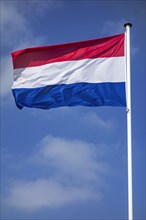 Dutch national flag of the Netherlands on flagpole flying in the wind against cloudy sky
