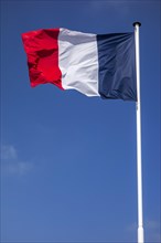 French national flag of France on flagpole flying in the wind against blue sky